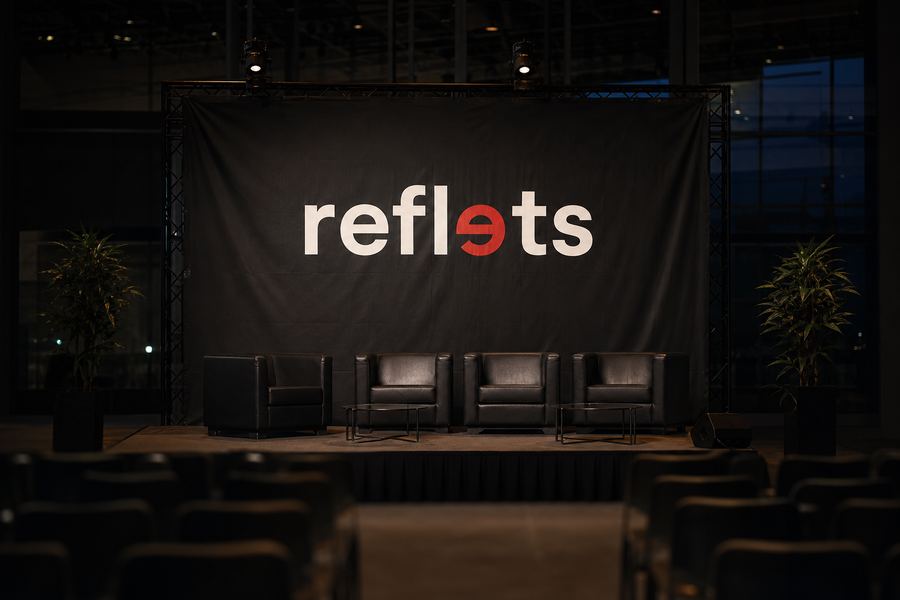 Grand fond de scène en textile mat sombre portant le logo Reflets, suspendu derrière une petite scène dans un hall d'exposition sous projecteurs