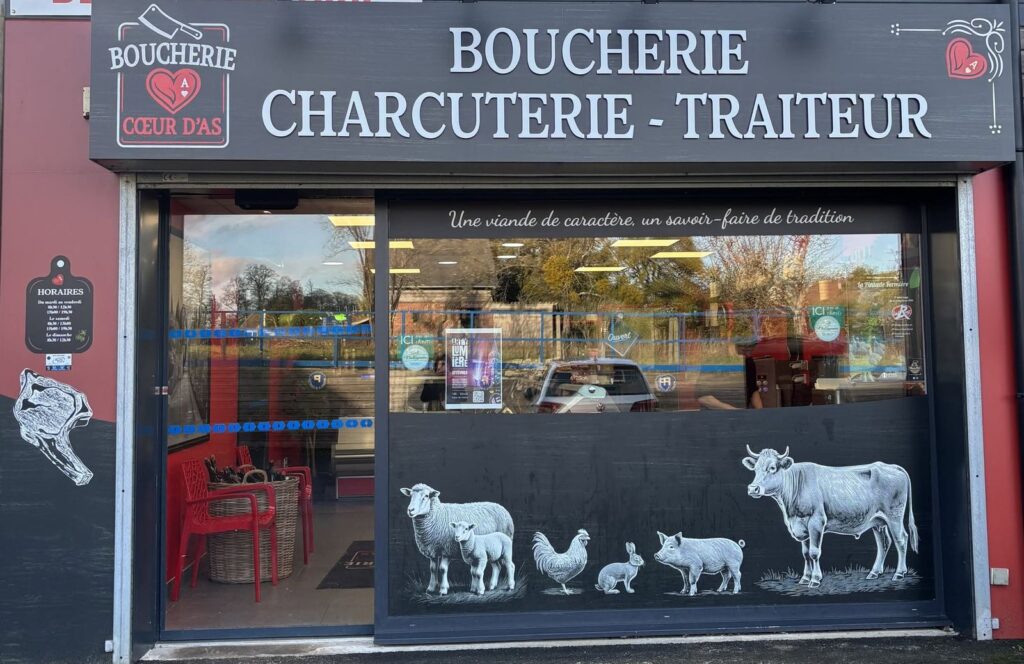 Enseigne bandeau anthracite avec lettres blanches en relief « Boucherie Charcuterie Traiteur », logo Cœur d'As et vitrophanie d'animaux de la ferme, réalisée par Refletscom