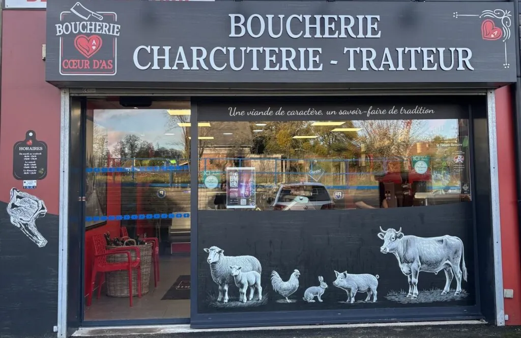 Enseigne bandeau anthracite avec lettres blanches en relief « Boucherie Charcuterie Traiteur », logo Cœur d'As et vitrophanie d'animaux de la ferme, réalisée par Refletscom