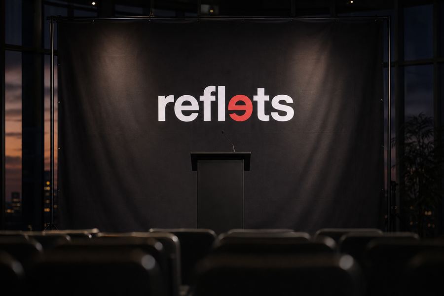 Fond de scène en tissu noir mat portant le logo Reflets derrière un pupitre vide sur une scène de conférence, rangées de sièges floues