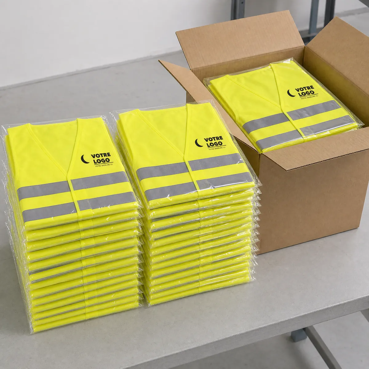 Piles de gilets jaunes personnalisés au logo, pliés en sachets individuels, et carton d'expédition ouvert