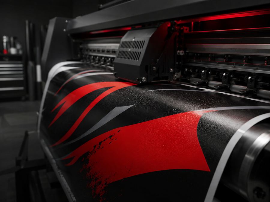 Imprimante grand format imprimant un visuel rouge et noir sur un rouleau de vinyle adhésif dans un atelier sombre