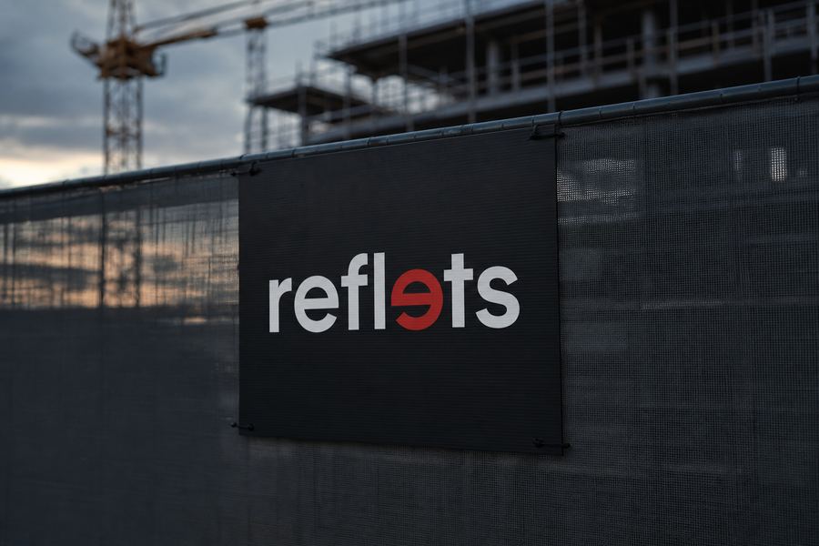 Panneau de chantier noir en Akilux portant le logo Reflets, fixé par colliers sur un grillage de chantier, grue et échafaudage en arrière-plan
