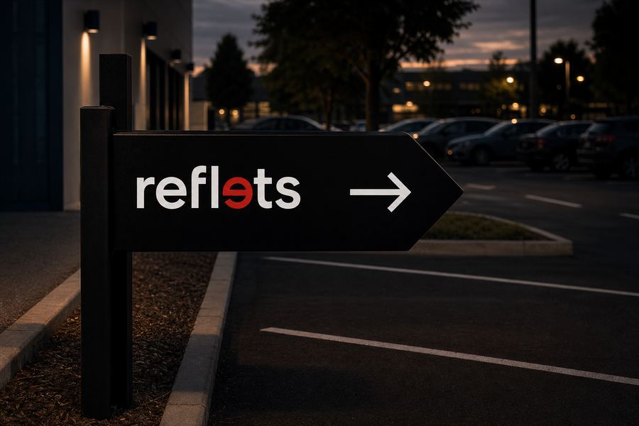 Panneau directionnel noir en forme de flèche portant le logo Reflets et une flèche blanche, fixé sur un poteau en bord de parking d'entreprise au crépuscule