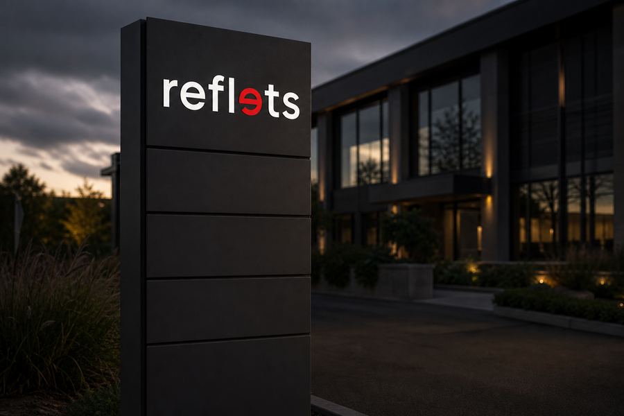 Grand totem gris foncé à l'entrée d'un centre d'affaires, face divisée en lames horizontales, la lame supérieure portant le logo Reflets, les autres vierges