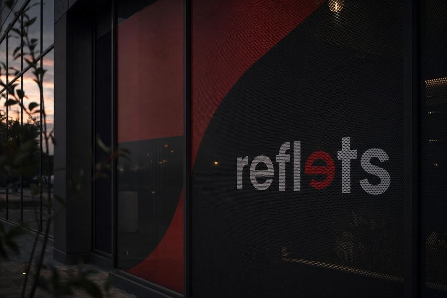 Grande façade vitrée recouverte d'un film microperforé imprimé rouge et anthracite avec le logo Reflets, trame de perforations visible, intérieur perceptible à travers les trous